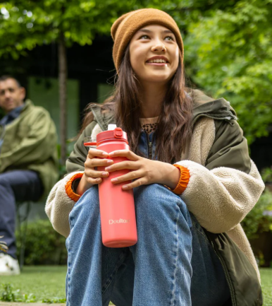 A girl holidng a peach Doulton bottle while out ona picnic