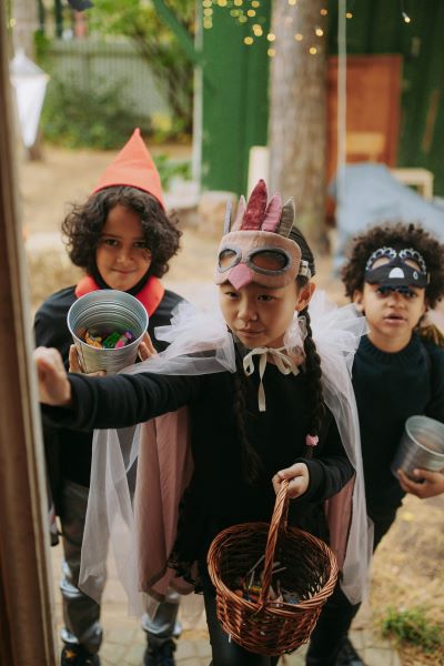 Three children in Halloween costumes others holding buckets and one holding a basket with candy