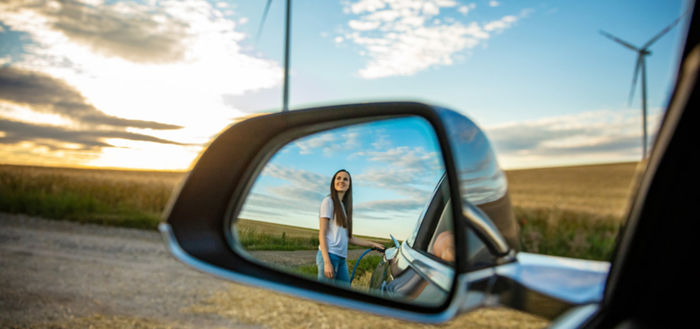 Spiegelbild einer Frau im Rückspiegel eines Auto in einer sonnigen Landschaft