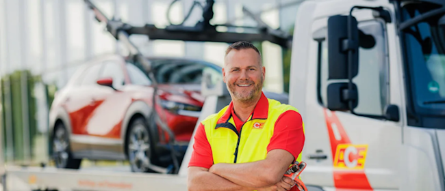 Ein Mitarbeiter der ACE-Pannenhilfe mit verschrenkten Armen und einem Lächeln vor einigen Fahrzeugen