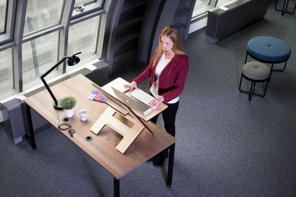 A woman standing at a height-adjudtable desk with hands on an open laptop