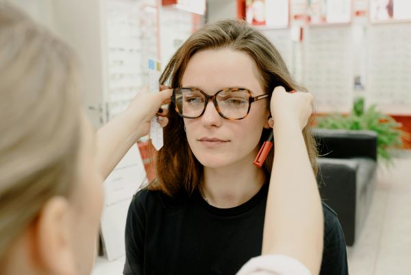 A woman in an optical store trying on eyeglasses while an optician adjusts them