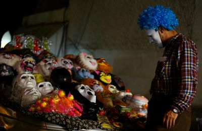 A man wearing a scary mask looking at more scary masks on a table