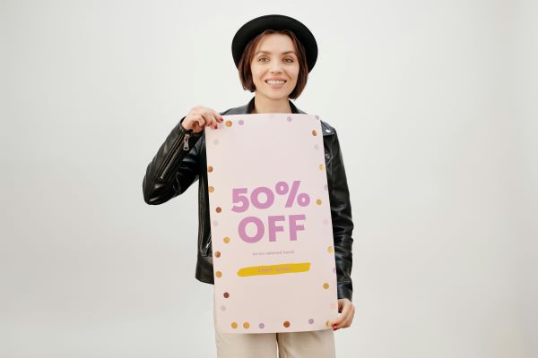 A woman wearing a leather jacket smiling while holding a 50% off sale sign