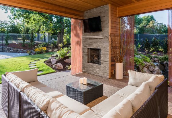 A patio with a stone foreplace and wall-mounted TV and a backyard with a lawn
