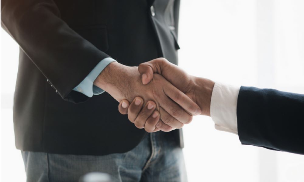 two hands wearing black suits shaking on a white background
