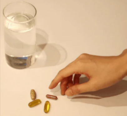 A person drinking different supplements from Higher Nature and a glass of water