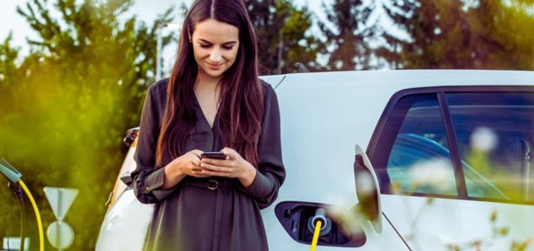 Eine lächelnde Frau vor einem Fahrzeug, die auf ihr Smartphone schaut