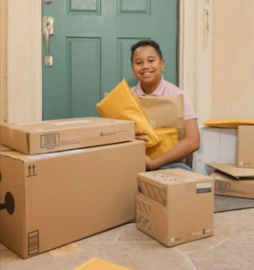 A boy sitting on a porch holding parcels bought on Amazon Prime Day