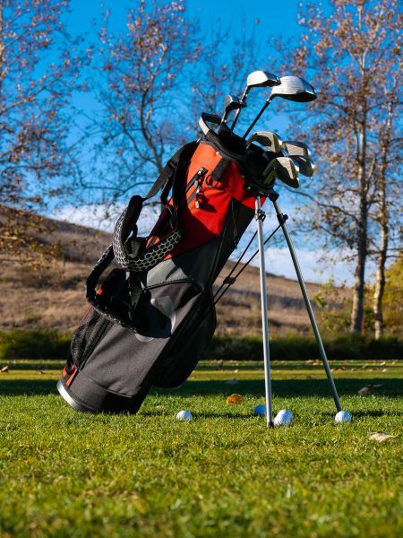 A red and black golf bag with clubs standing on a grassy course with golf balls nearby
