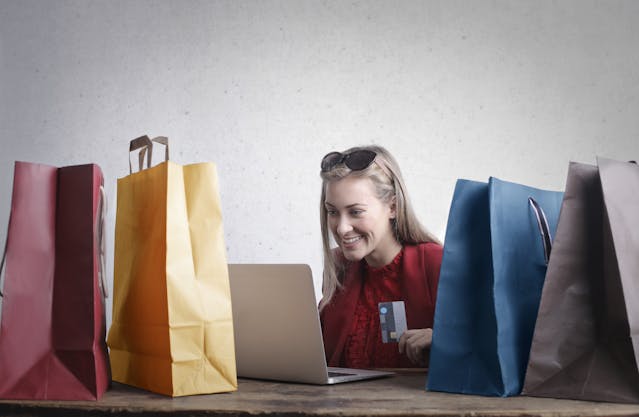 A woman with a credit card and shopping bags using a laptop to shop Labor Day sales