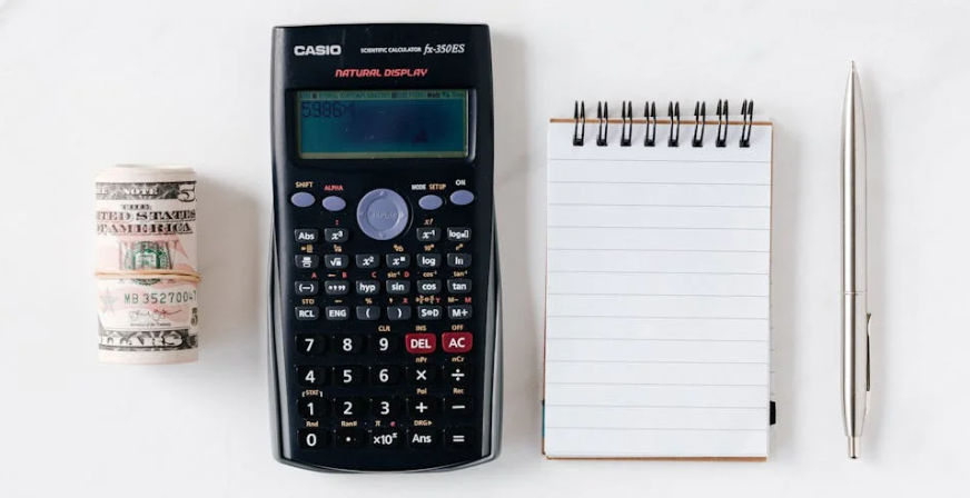 casio scientific calculator next to money, notepad and a pen showcasing the idea of 'budgeting' and saving money