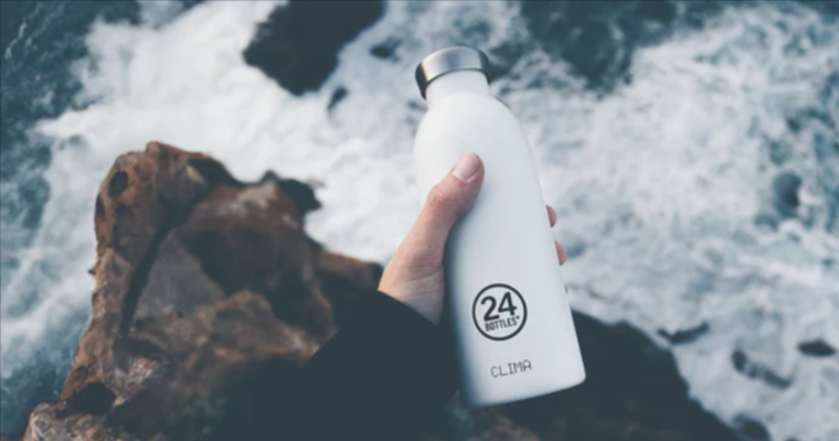 A hand holding a white bottle with a silver lid and a 24Bottles logo