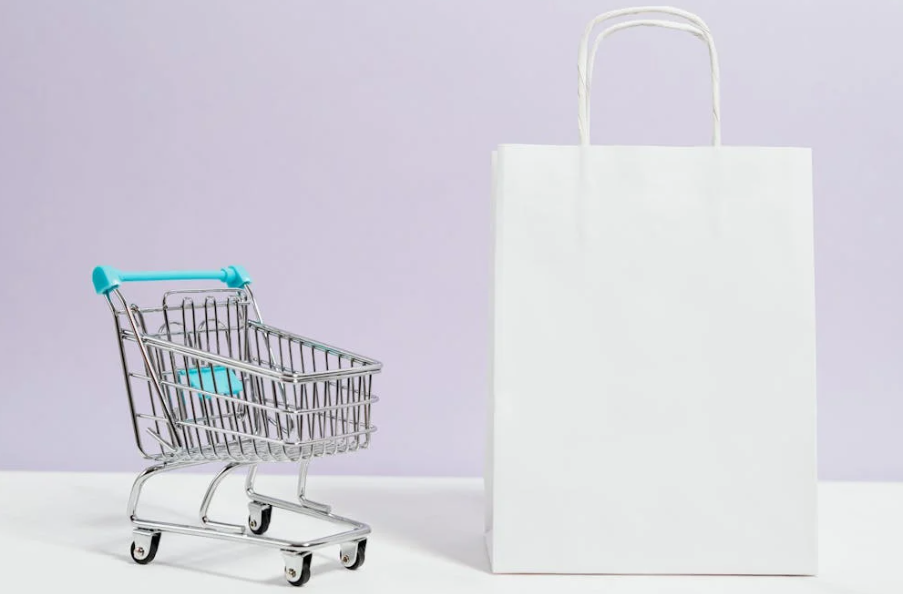 Novelty mini shopping cart next to a white paper bag gift bag with a purple background