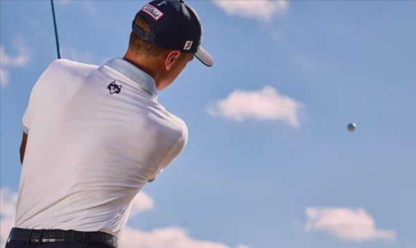 A young man playing golf wearing a white golf t-shirt and a navy blue cap