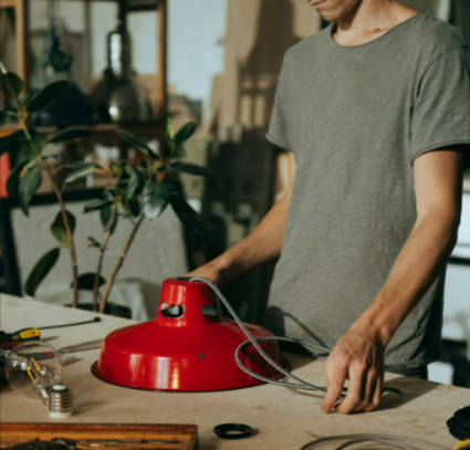 Craftsman working on a lamp repair with tools from Frost in a workshop, focusing on electric wiring skills.