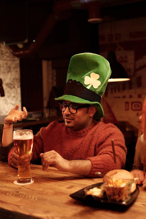 A person wearing a big green hat while drinking alcohol