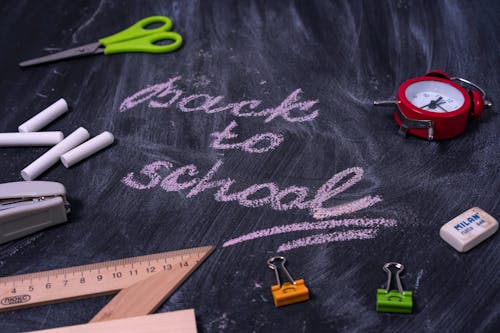 The words "Back to School" written on a chalk board surrounded by stationery and school supplies