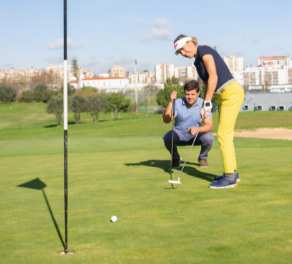 Golfers practicing putting on a sunny day with a city backdrop.