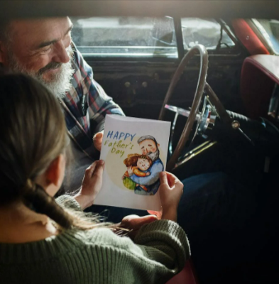 Woman in grey sweater sitting on red leather car seat gifting her dad a Father's Day card