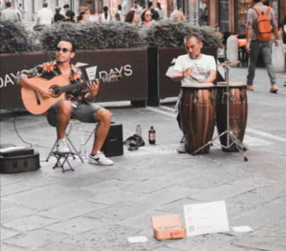 Buskers playing instruments bought from Gear4music on a lively city street, attracting a crowd of pedestrians.