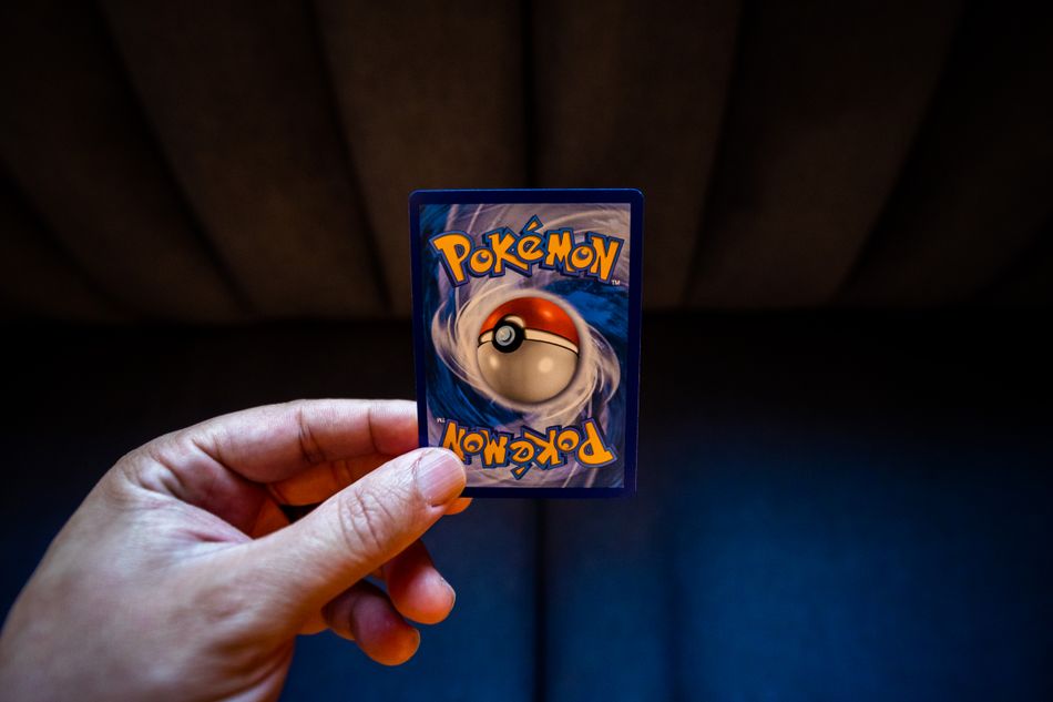 A hand holds a Pokémon trading card with a dark background