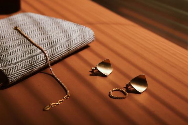 Gold jewellery set with a necklace, earrings, and a ring next to a herringbone pouch on a wooden surface
