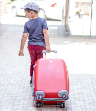 A young boy in a grey shirt and red pants pulling a suitcase bought from Go Places outdoors.
