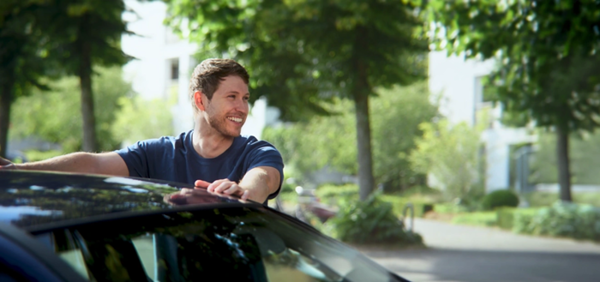 Ein lächelnder Mann mit seinen Händen auf einem Auto mit Bäumen im Hintergrund