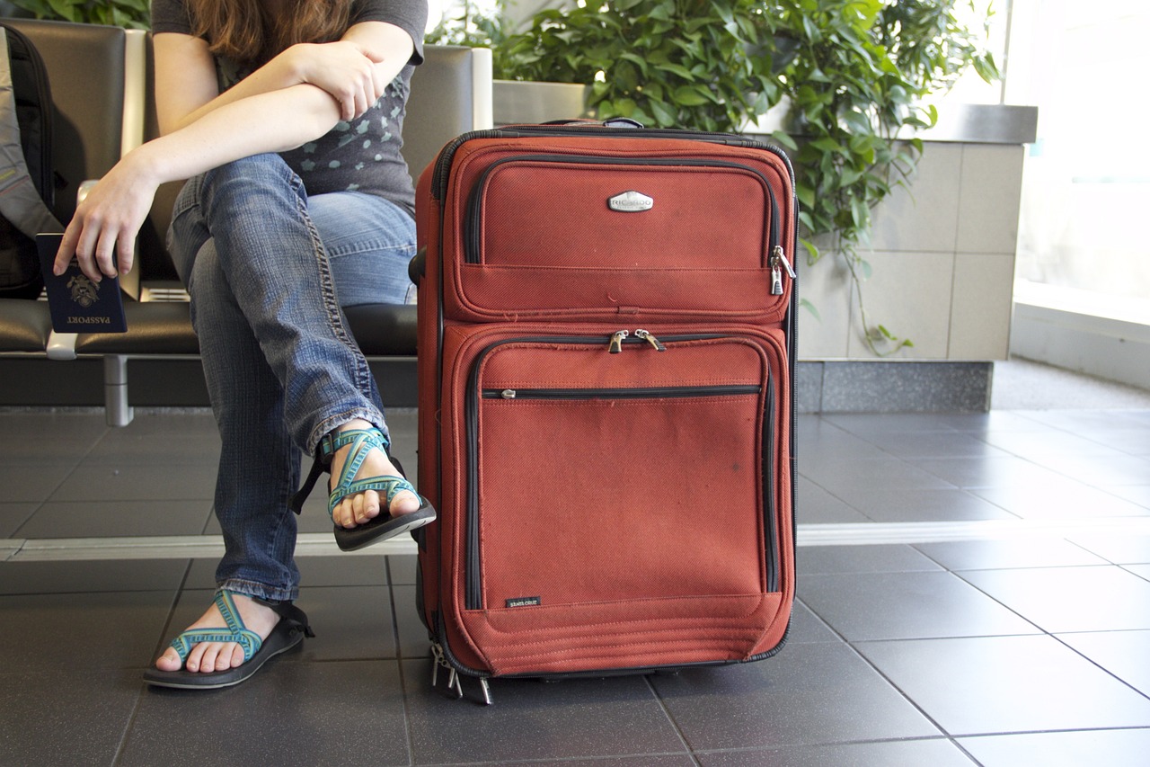 persona sentada en aeropuerto con maleta granate