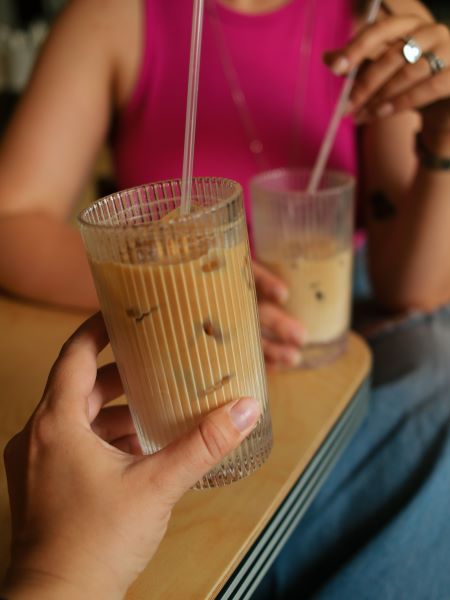 Two people holding glassed of iced coffee with straws at a cafe table