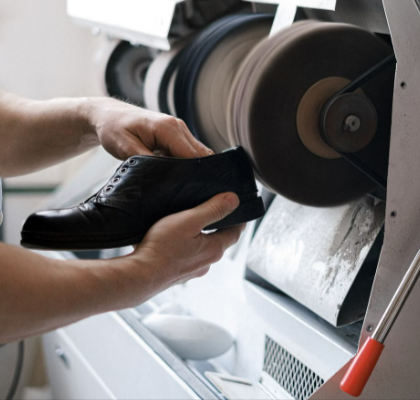 Close-up of craftsman polishing a Grenson leather shoe using industrial machinery indoors.