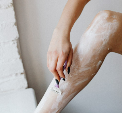 Woman shaving her leg with foam using a razor from Gillette during her personal grooming routine.