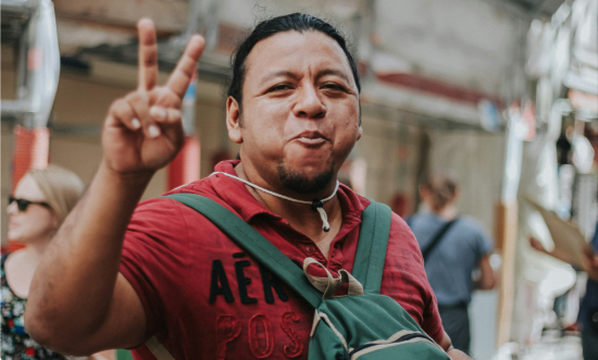 a Mexican man eating food, making a peace sign with his fingers