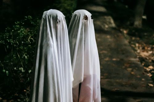 Two children posing in ghost costumes for Halloween that they saved on with a Halloween promo code