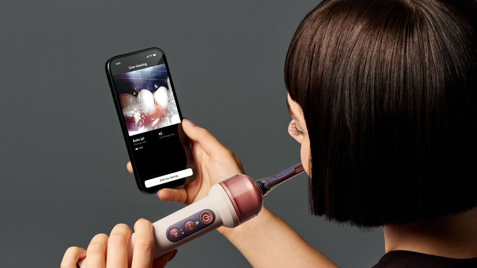 A woman brushing her teeth with the Dyson CameraJet toothbrush’s live viewing feature