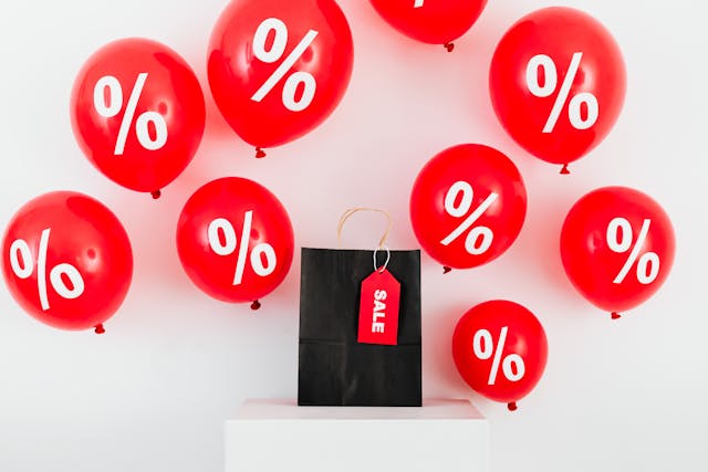 A black shopping bag on a table surrounded by red percentage sign balloons.