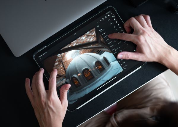 Hands editing a photo of a domed building on a tablet using photo editing software