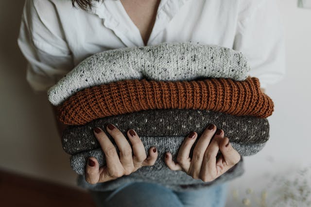 A woman holding folded knitwear from an autumn capsule wardrobe