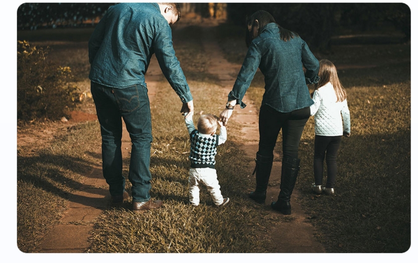 Family walking outdoors holding hands with their young children.