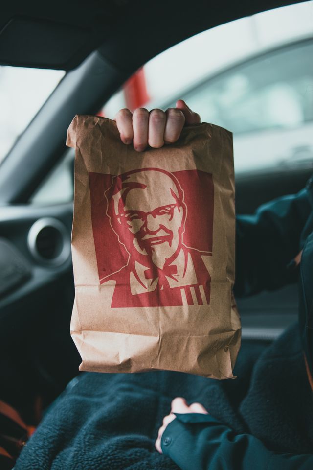 A person holds a KFC paper bag inside a car