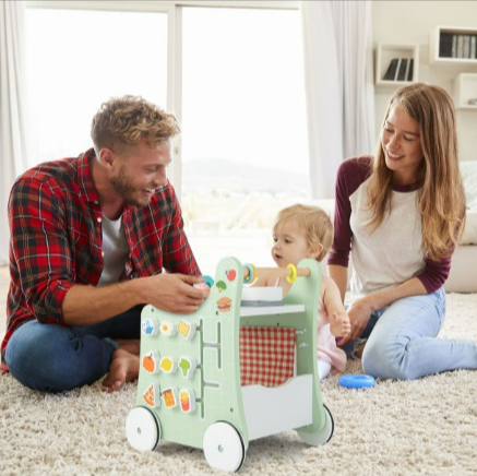 A baby playing with a walker in a playroom with their parents
