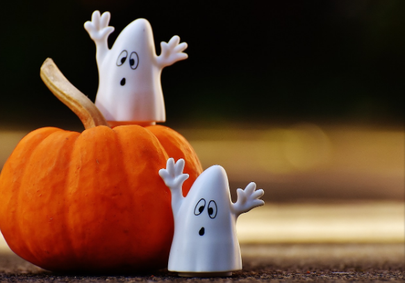 Dos juguetes de fantasmas uno encima de una calabaza y otro a un costado sobre un escritorio