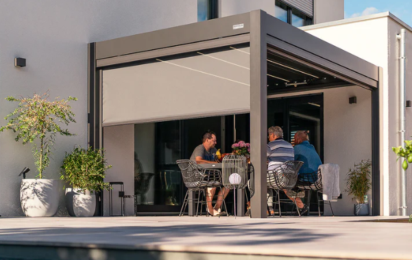 An image of the latest Pergolux Skydance S2 on a garden deck patio and three men seated under the pergola