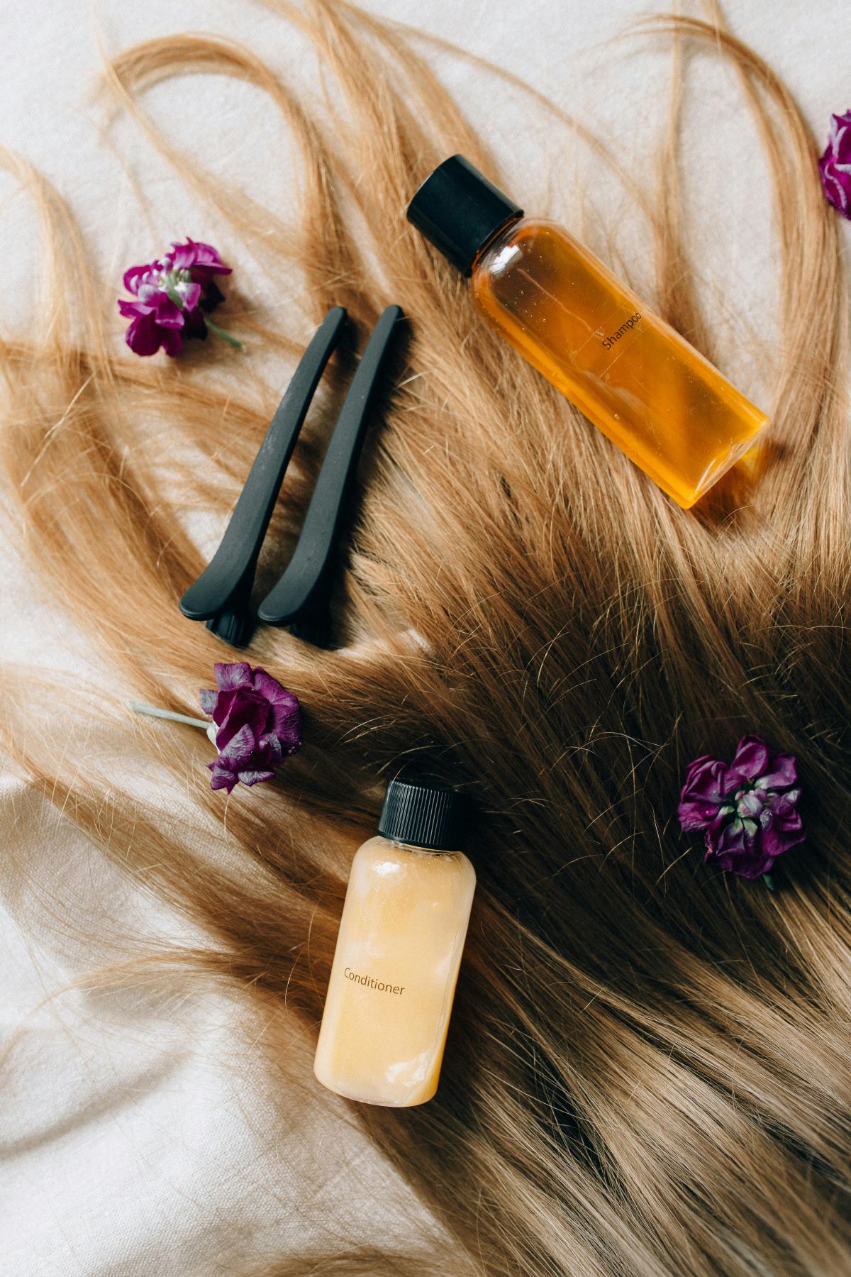 Hair conditioner, shampoo, and hair clips are placed on long hair on a flat surface.