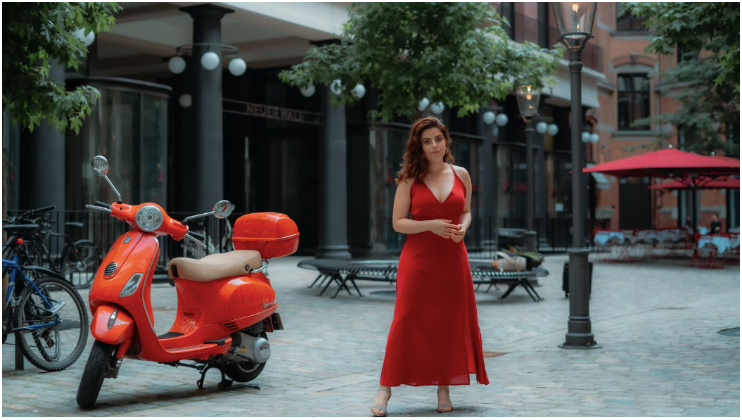 A young woman wearing a fiery red dress is standing in front of an orange scooter