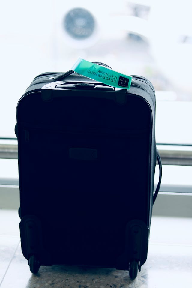 A black large luggage suitcase with a green “Approved Cabin Luggage” on the handle in an airport