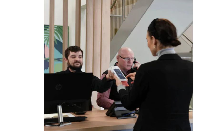 lady in a black suit holding a card machine in front of two gentlemen who are seated behind a desk