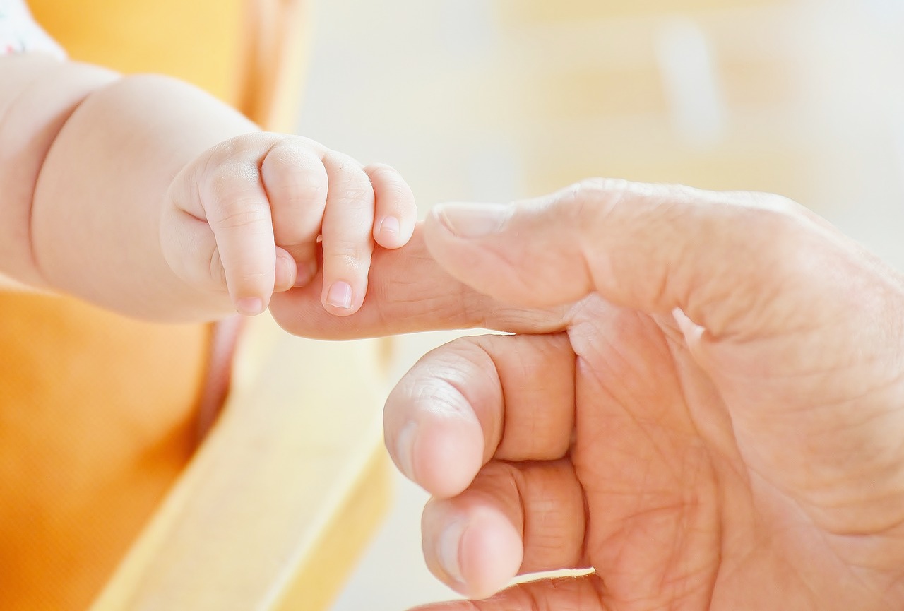 imagen de la mano paternal tocando el dedo de un bebe recién nacido con fondo luminoso