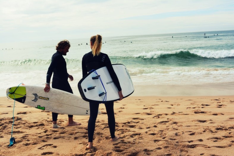 coppia di surfisti che entra in acqua mentre usa delle mute di immersione acquistate a buon prezzo grazie ai promo code Billabong